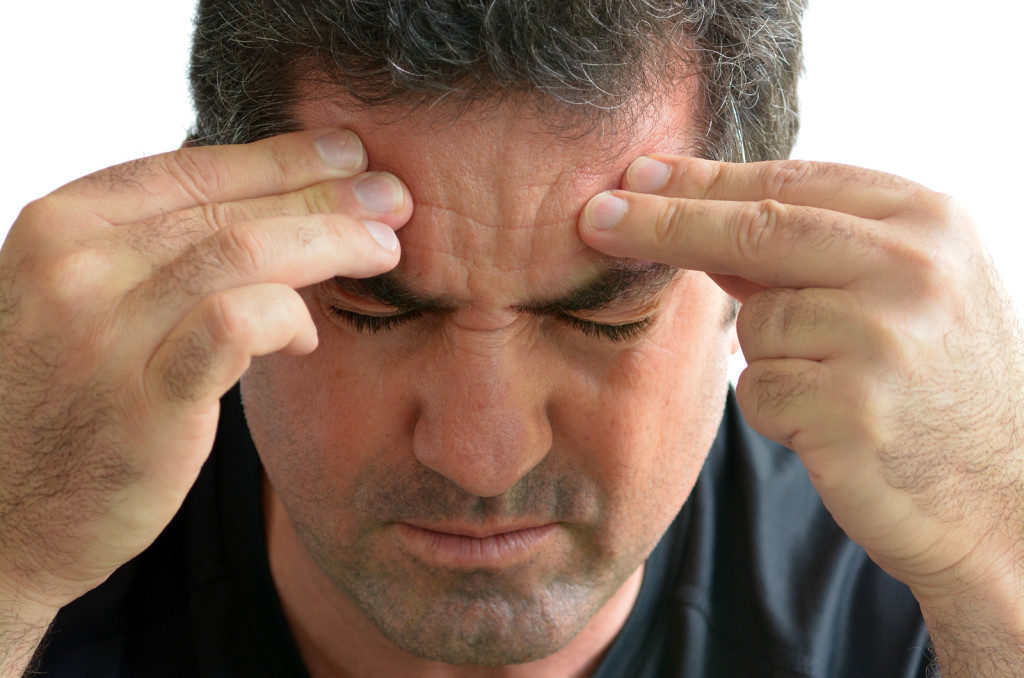 A man experiencing a headche, he is closing his eyes while he pinches his forehead with both hands.
